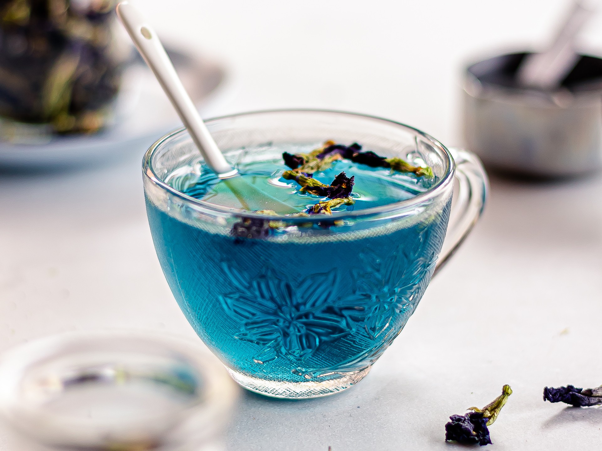 Blue butterfly pea flower tea in a glass cup with dried flowers